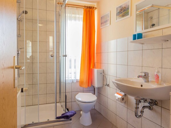 Et badeværelse med glasbrusekabine, toilet, vask og spejl.