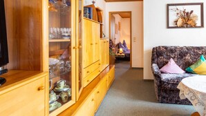 Ein gemütliches Wohnzimmer mit einer Holzkabine, die Glaswaren und Keramik zeigt, einer geprägten Couch mit Kissen und einem gerahmten Kunstwerk an der Wand.
