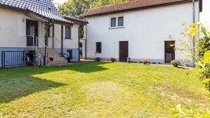 Ein zweistöckiges Haus mit überdachter Veranda, einem Fahrrad und einem gepflegten Rasen.