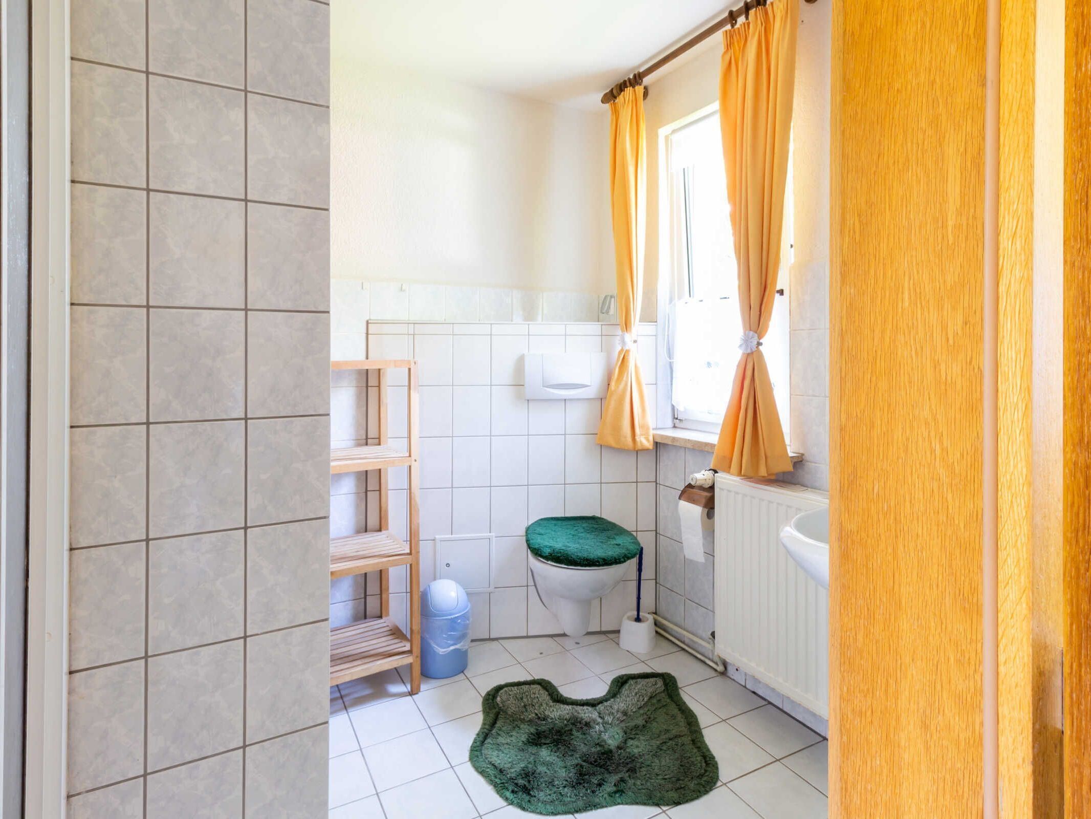 Un baño con inodoro, estante, radiador y alfombra verde.