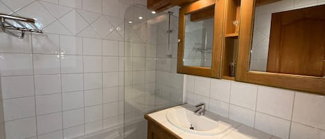 A bathroom with a glass-enclosed shower, a white sink, and wooden cabinets.
