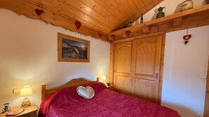 A cozy bedroom with a wooden ceiling, a bed with a heart-shaped pillow, a nightstand with a lamp, and a wooden wardrobe. - 3-room Apartment Les Saisies, 6 pers, balcony, 2 baths, ski locker (Les Saisies)
