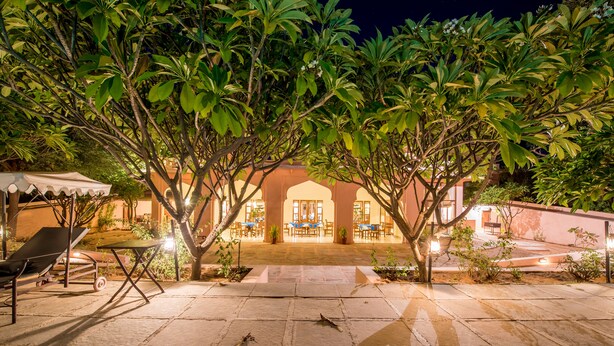 An outdoor patio area with stone flooring, lounge chairs, and a dining area with tables and chairs. - Hotel Dev Vilas (Sawai Madhopur)