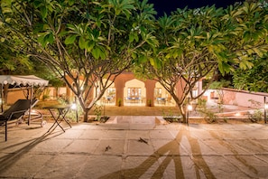 An outdoor patio area with stone flooring, lounge chairs, and a dining area with tables and chairs. - Hotel Dev Vilas (Sawai Madhopur)