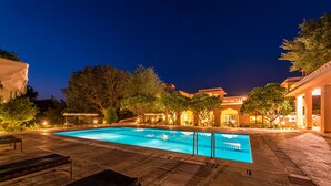 A nighttime swimming pool with lounge chairs and a covered area, surrounded by trees and buildings. - Hotel Dev Vilas (Sawai Madhopur)