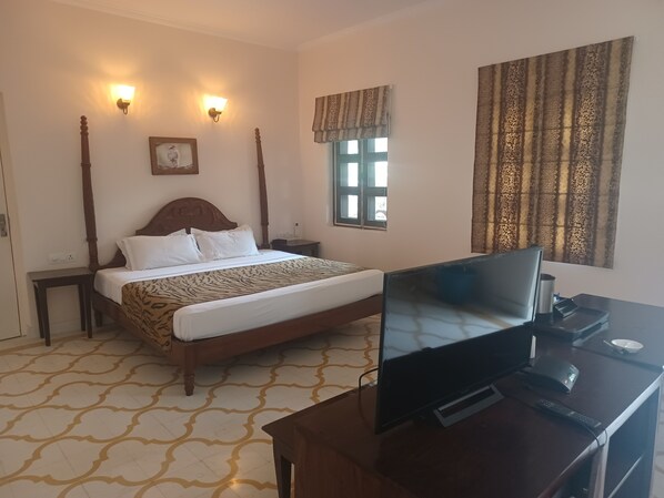 Una habitación de hotel con cama, mesitas de noche, un escritorio con computadora, una ventana con cortinas y luces fijadas a la pared.