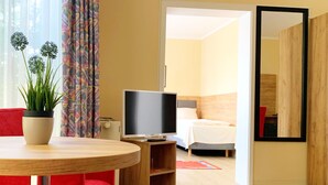 Une chambre d’hôtel avec un lit, une télévision, une petite table avec une plante et une chaise rouge.
