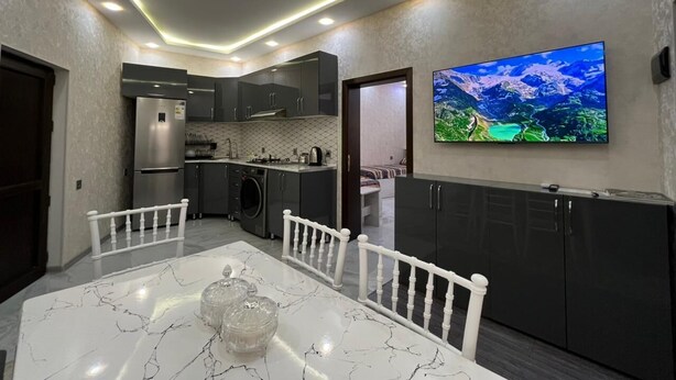 A modern kitchen with built-in appliances, a dining area with a marble table, and a large flat-screen TV mounted on the wall. - VM Hostel (Ganja)