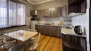 A modern kitchen with wooden cabinets, a dining area with a table and chairs, and a built-in oven. - VM Hostel (Ganja)