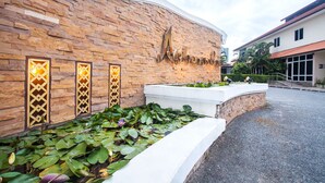 A building with a stone facade, a large sign, and a water feature with lotus plants. - Achawalai By PP (Pattaya)