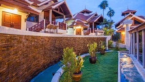 A traditional-style building with multiple levels, a stone wall, and a small garden area with potted plants. - Achawalai By PP (Pattaya)