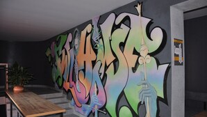 A modern interior with a colorful graffiti wall, a wooden table, and a staircase. - Full House Capsule Hostel (Rivne)