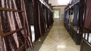 A corridor with bunk beds and curtains, leading to a door with a patterned wall. - Sunshine Hostels (Mumbai)