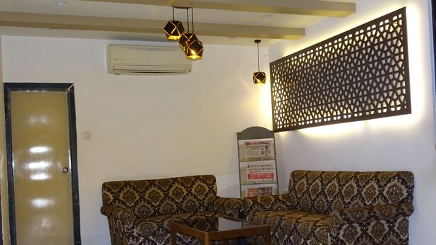 A room with two patterned sofas, a wooden coffee table, a decorative wall panel, and a signboard. - Sunshine Hostels (Mumbai)