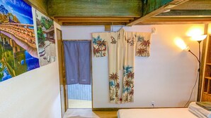 Una habitación con piso de madera, dos camas, una cortina con motivos tropicales y un cuadro de un puente.