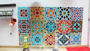 Una habitación con una pared de azulejos coloridos, una lámpara colgante y un pequeño estante con objetos.