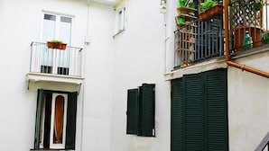 Un edificio blanco con un balcón, una ventana con contraventanas verdes y una puerta con marco blanco.
