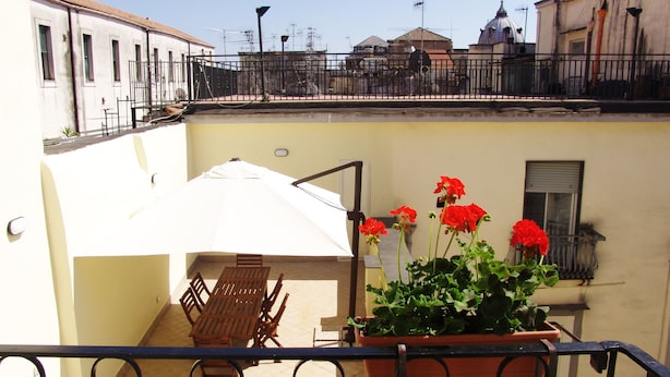 Un balcón con una mesa y sillas, una planta en maceta con flores rojas y un paraguas blanco.