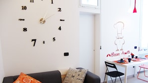 Un espacio de estar con un sofá, un reloj de pared, una mesa de comedor y una silla.