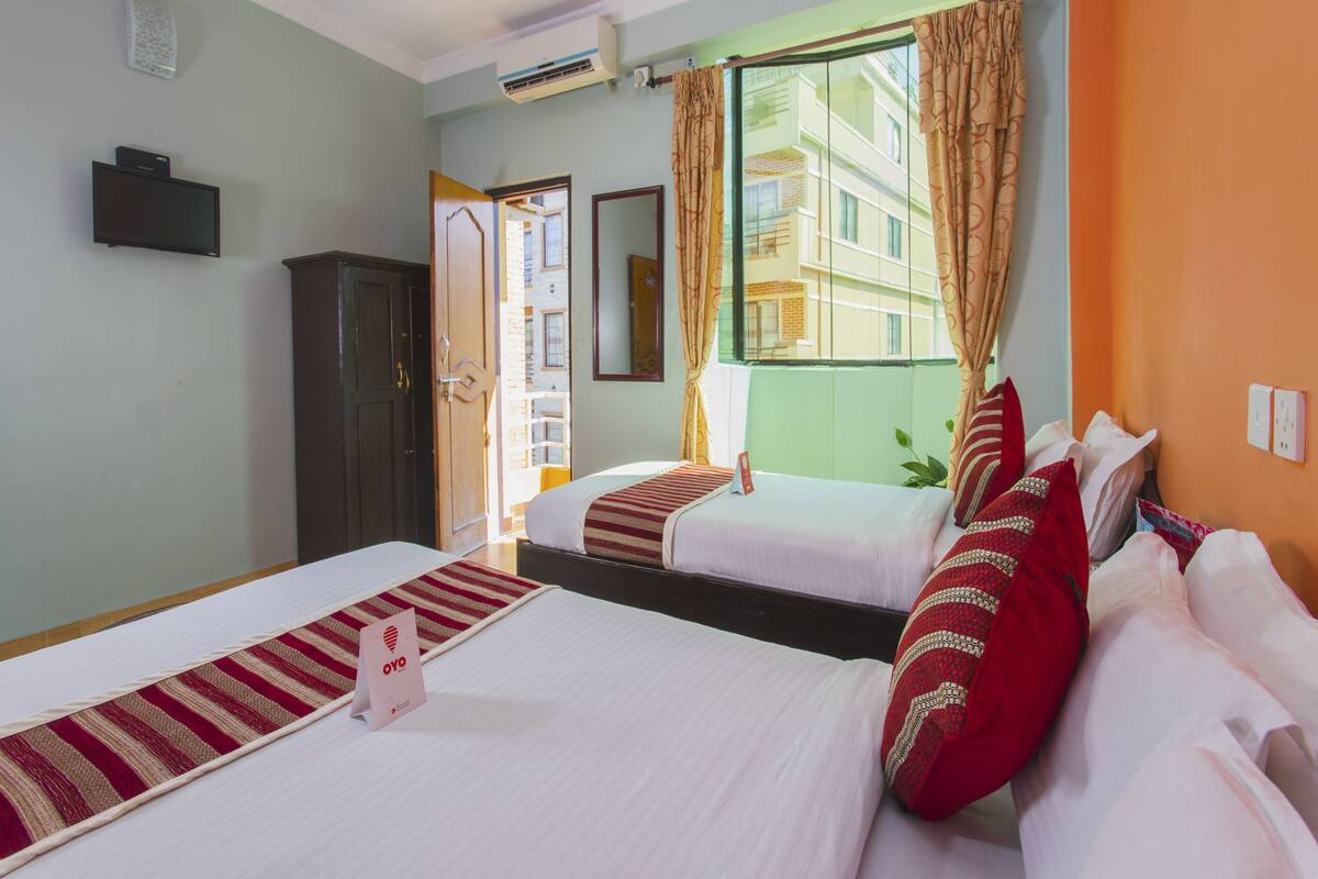 A hotel room with two beds, a large window with curtains, a ceiling fan, and an air conditioning unit.