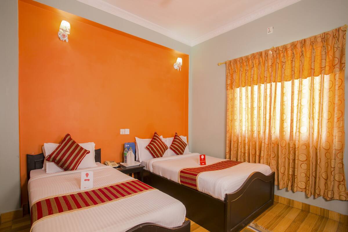 A hotel room with two beds, orange walls, a window with curtains, and a wooden floor.