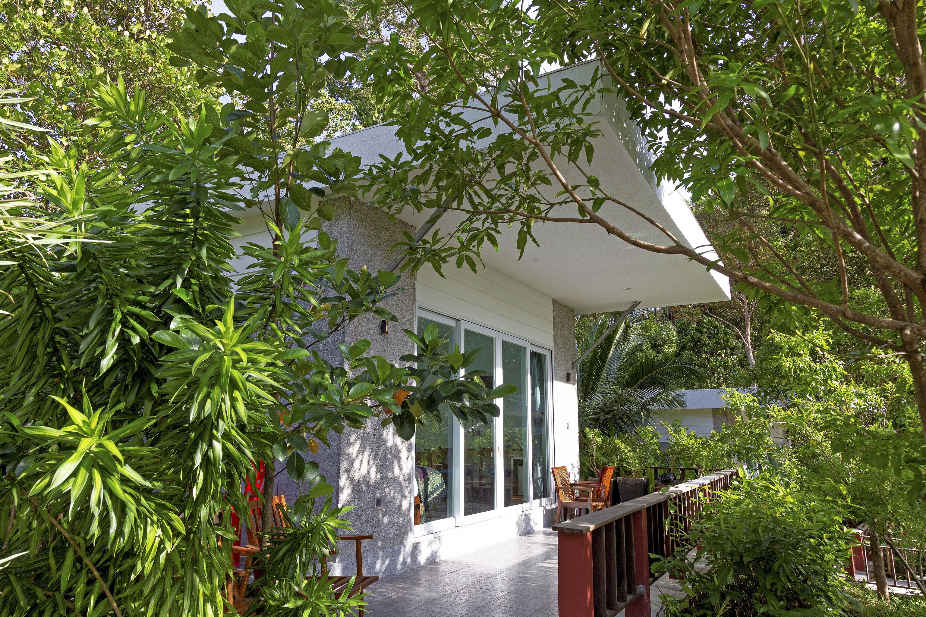 Uma casa moderna com varanda coberta, rodeada por vegetação exuberante.