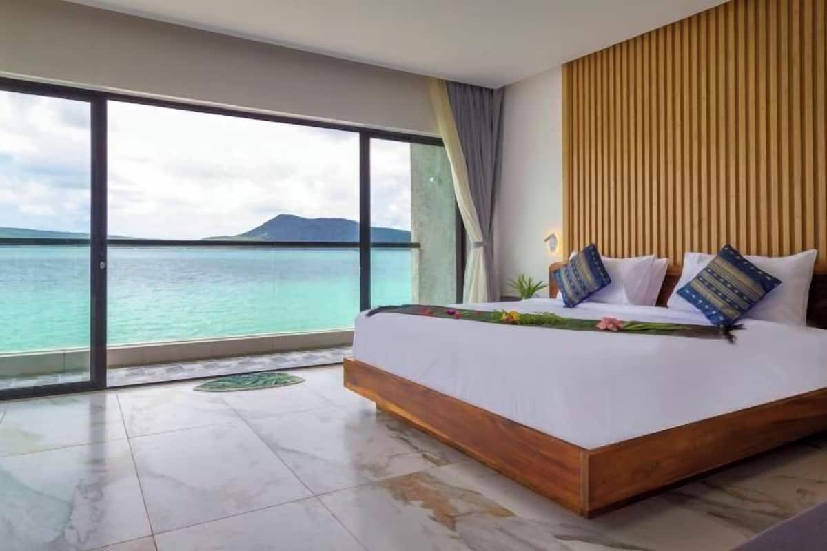 A bedroom with a large bed, a view of the sea, and a wooden headboard.
