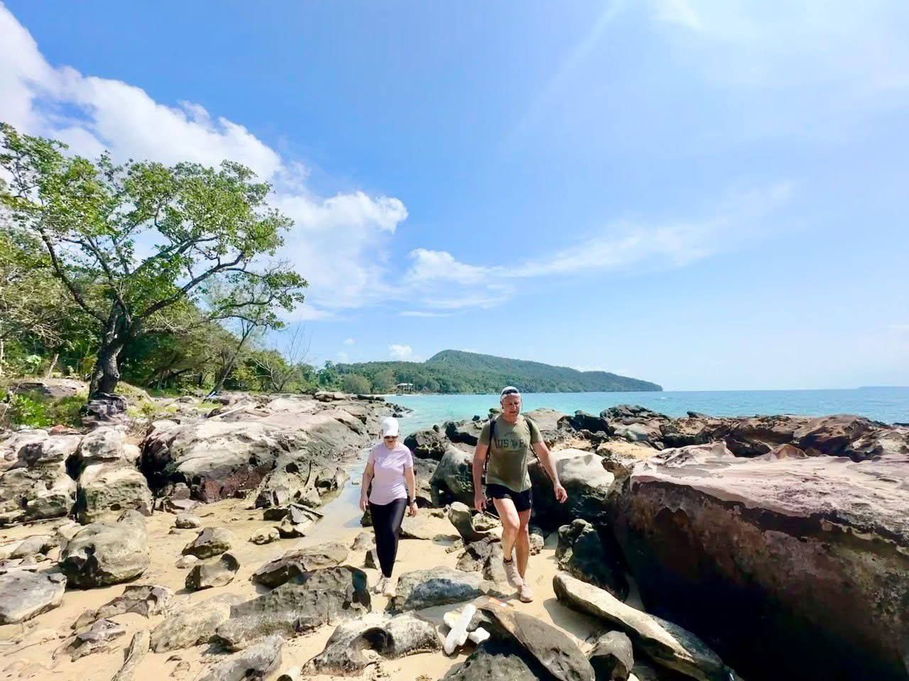 Two people walking on rocky terrain with a body of water and a distant island in the background.