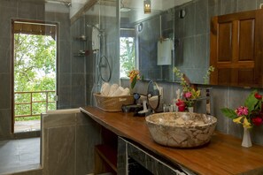 A modern bathroom with a large mirror, a wooden countertop, a stone basin, and a shower area.