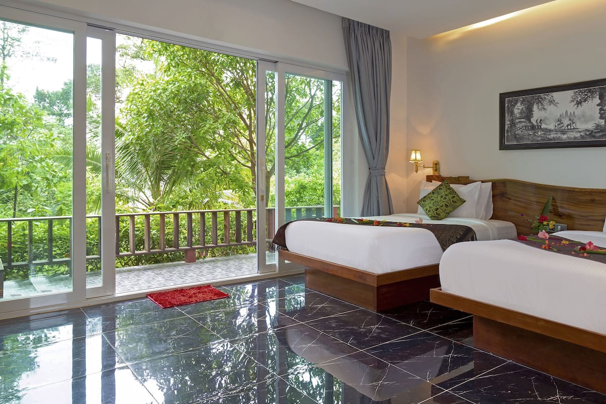 A hotel room with two beds, a balcony, and a large window with a view of greenery.
