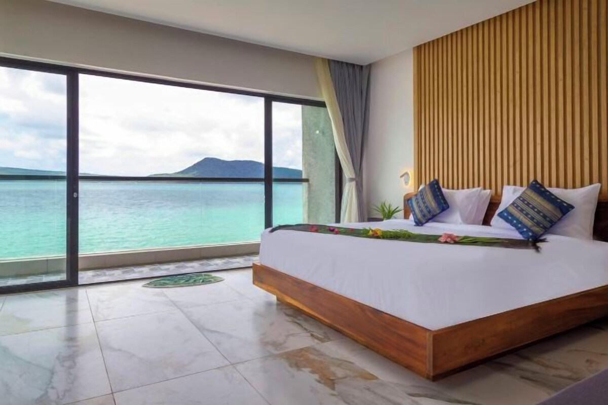 A bedroom with a large bed, a view of the sea, and a wooden headboard.