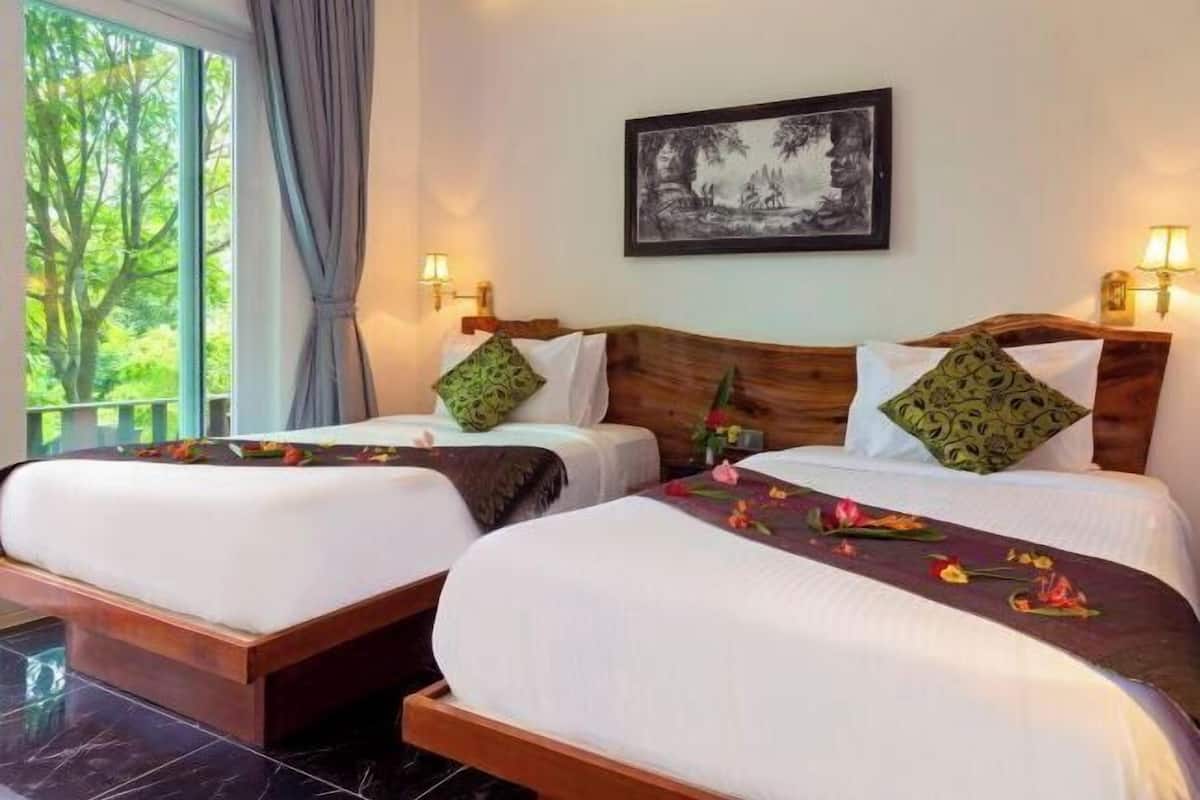 A hotel room with two beds, a large window with a view of trees, a framed picture on the wall, and wall-mounted lamps.