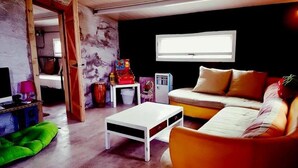 A cozy living room with a sofa, a coffee table, and a television. There is a window providing natural light and a door leading to another room. - Kenting Sky Villa (Hengchun)