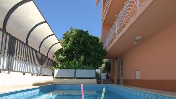 En swimmingpool med to drikkevarer, et overdækket område og en bygning med balkon.