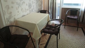 Ein Essbereich mit einem Tisch, der mit einer weißen Tischdecke bedeckt ist, umgeben von vier Stühlen mit braunen Kissen. Der Raum hat raumhohe Tapete und einen Teppich mit Muster auf dem Boden.