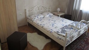 Ein Einzelbett mit blumigem Überwurf, ein Nachttisch mit Lampe und ein weißer Teppich auf Holzdielen.