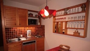 Eine kleine Küche mit Holzausstattung, einer Mikrowelle, einem Spülbecken und einer roten Tischdecke.