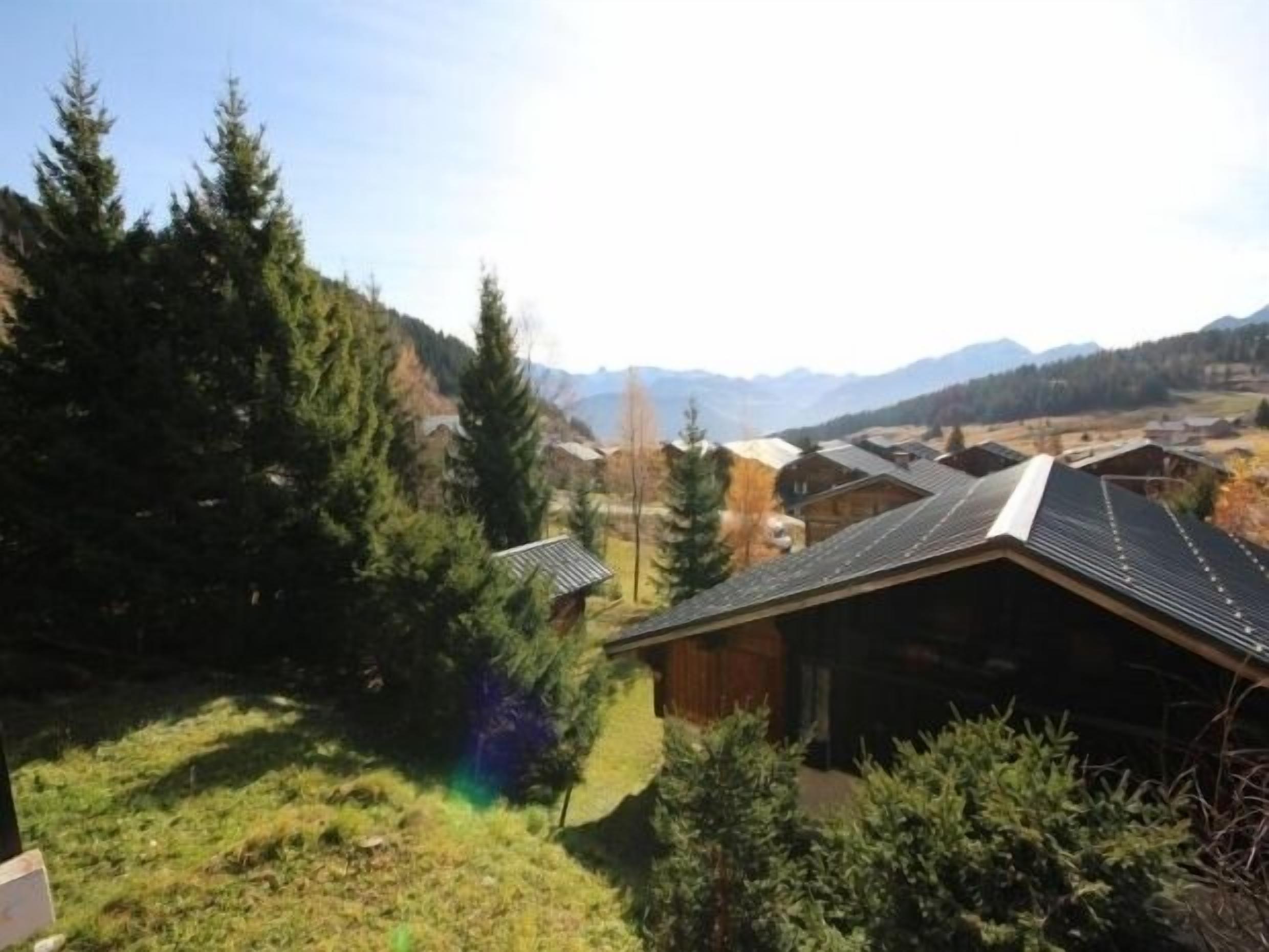 A rural cabin with a sloped roof, surrounded by dense forest and mountains in the background.