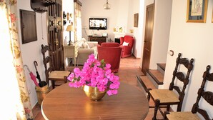 A dining area with a round wooden table, a brass bowl with pink flowers, and two wooden chairs with woven seats. - Casa Azul (Alozaina)