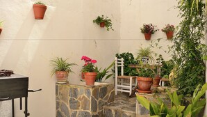 A stone bench with potted plants, a white chair, and a table with a metal cart. - Casa Azul (Alozaina)