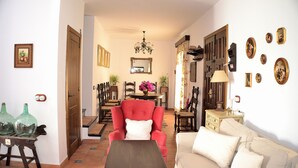 A living room with a red armchair, a beige sofa, a wooden coffee table, and a dining area with a chandelier. - Casa Azul (Alozaina)