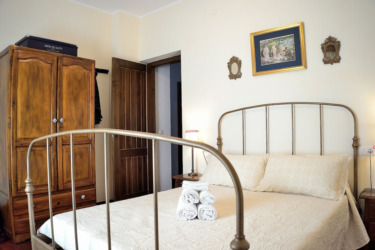 A bedroom with a metal bed frame, a wooden wardrobe, and a framed picture on the wall.