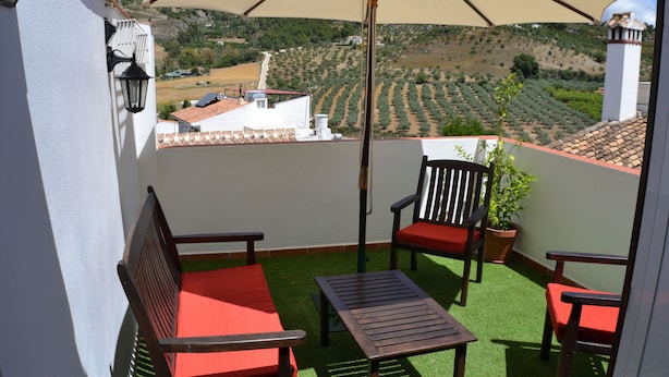 A balcony with a table and two chairs, a potted plant, and a large umbrella. - Casa Azul (Alozaina)