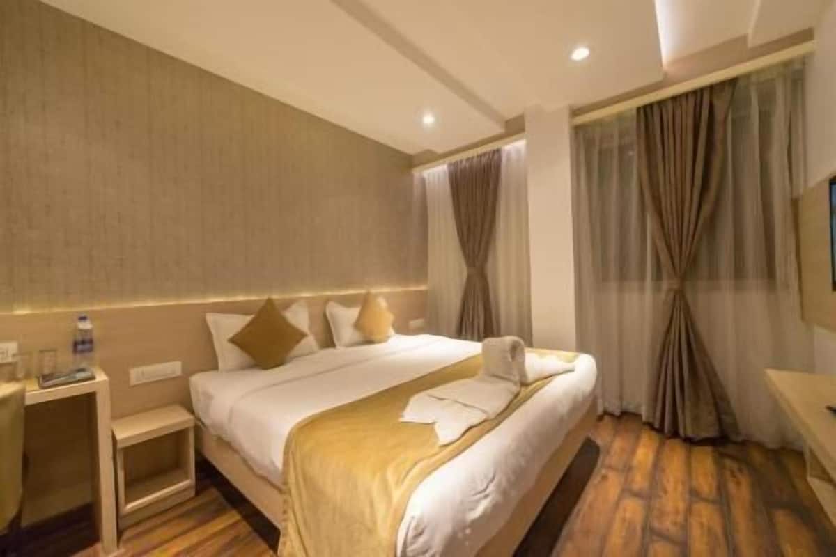 A hotel room with a bed, bedside tables, a desk, and a window with curtains.