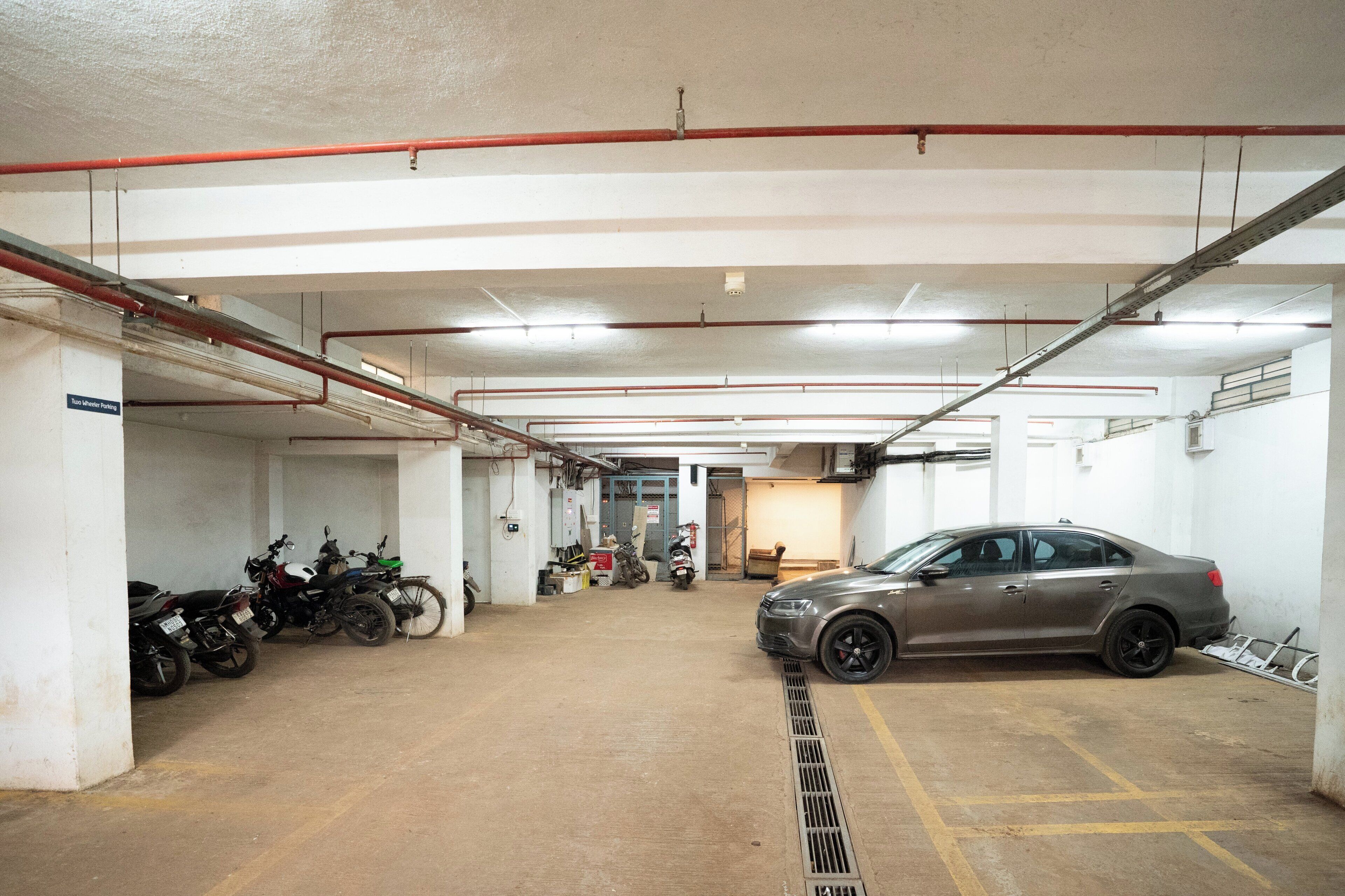 A parking garage with multiple motorcycles and a car parked.