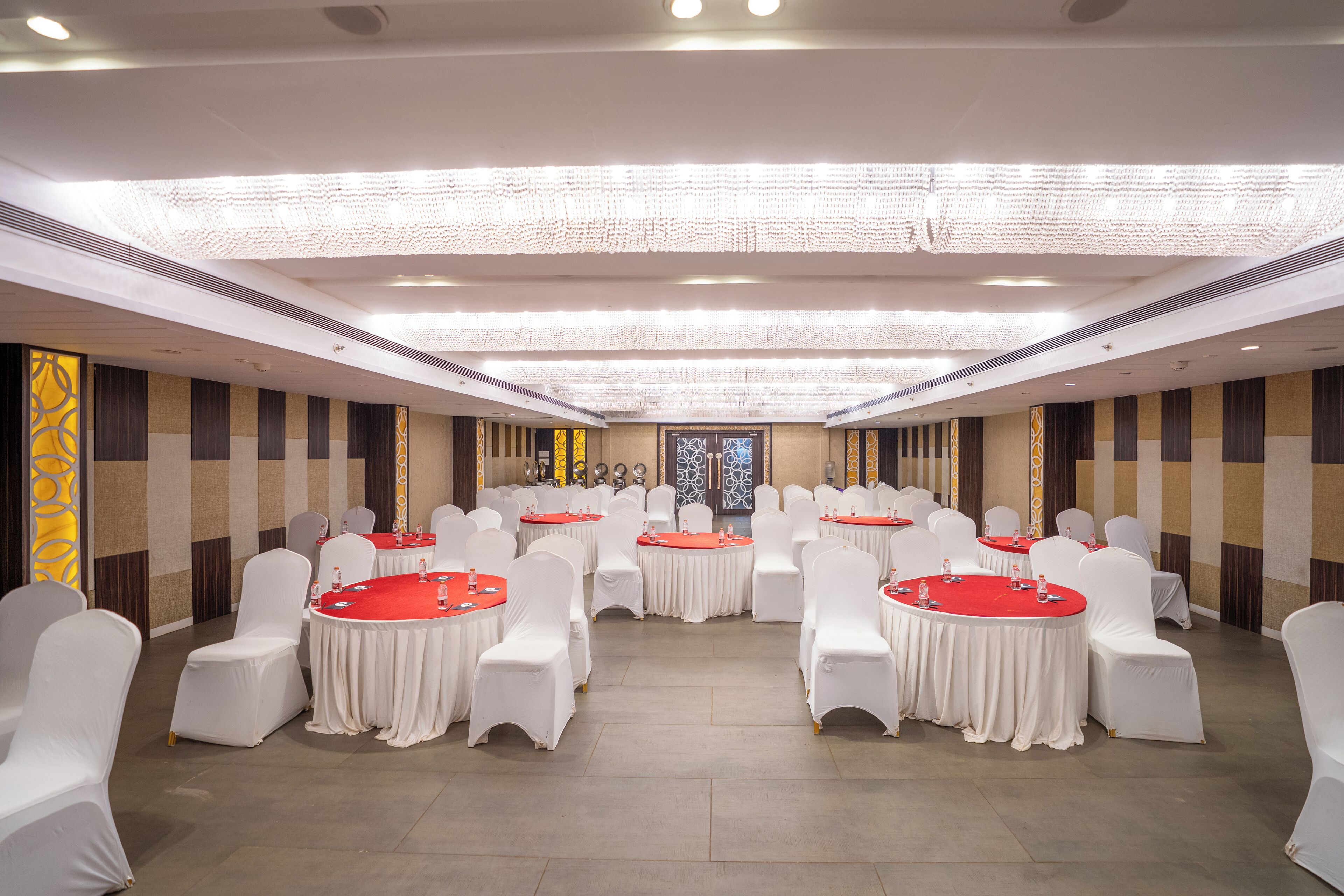 A banquet hall with round tables and white chairs, a chandelier, and a decorative wall with vertical stripes.