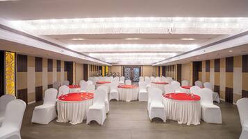 A banquet hall with round tables and white chairs, a chandelier, and a decorative wall with vertical stripes.