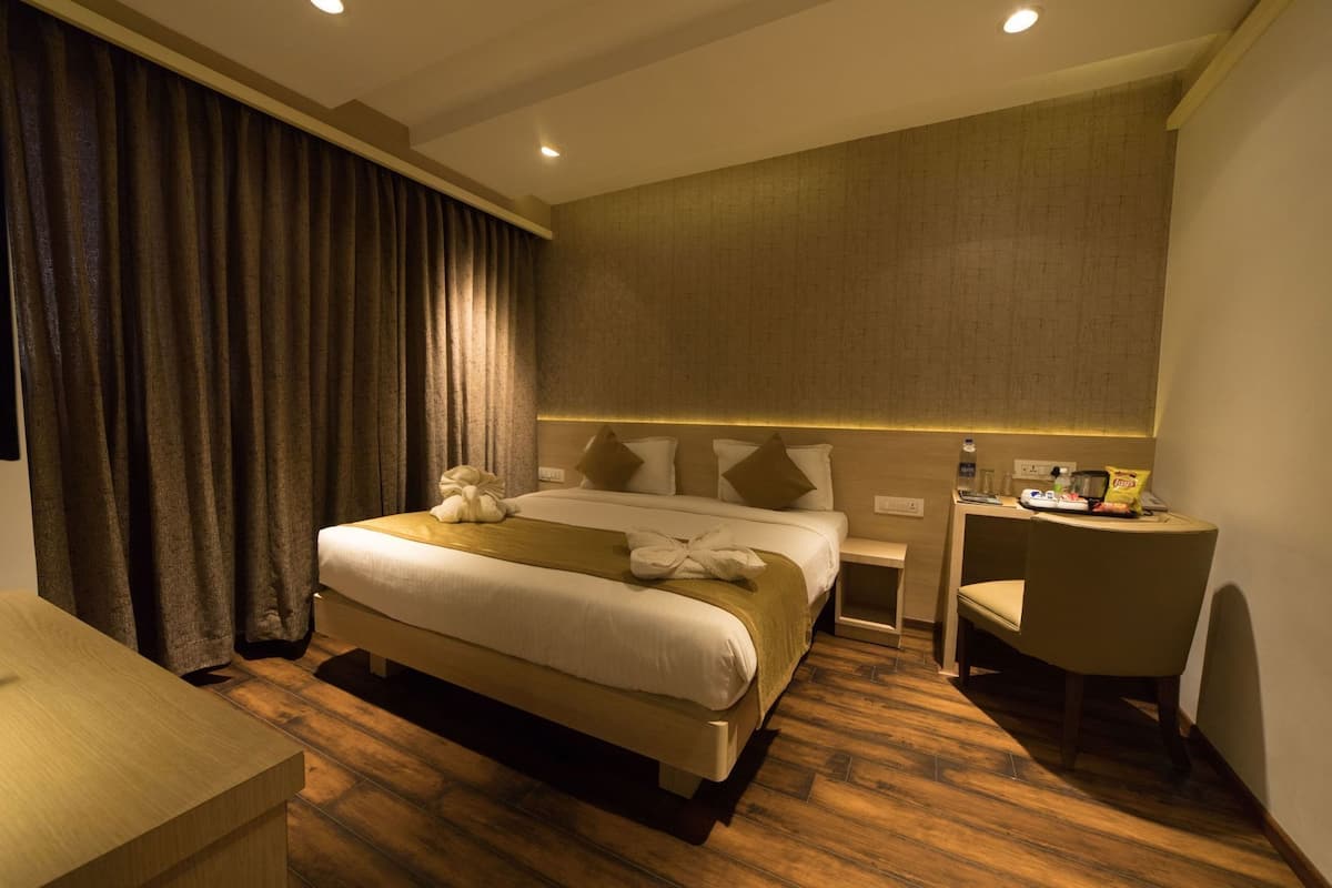 A hotel room with a large bed, a bedside table, a chair, and a desk.