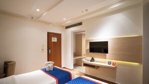 Habitación de hotel con dos camas, televisión, escritorio y una pequeña zona de estar.