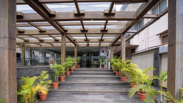 Una escalera techada al aire libre con plantas en macetas a ambos lados, que conduce a la entrada de un edificio.
